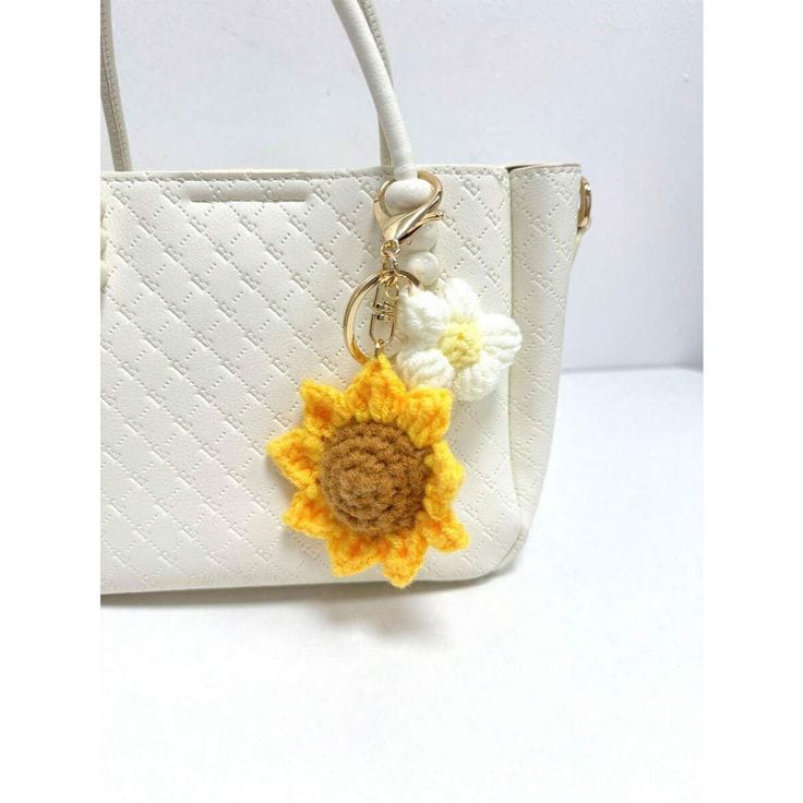 Handmade crochet sunflower bag charm with yellow petals and green leaves, hanging on a white tote with brown leather handle