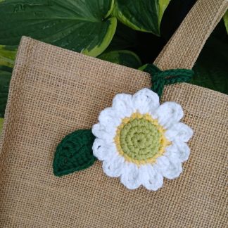 Handmade crochet sunflower bag charm with yellow petals and green leaves, hanging on a white tote with brown leather handle