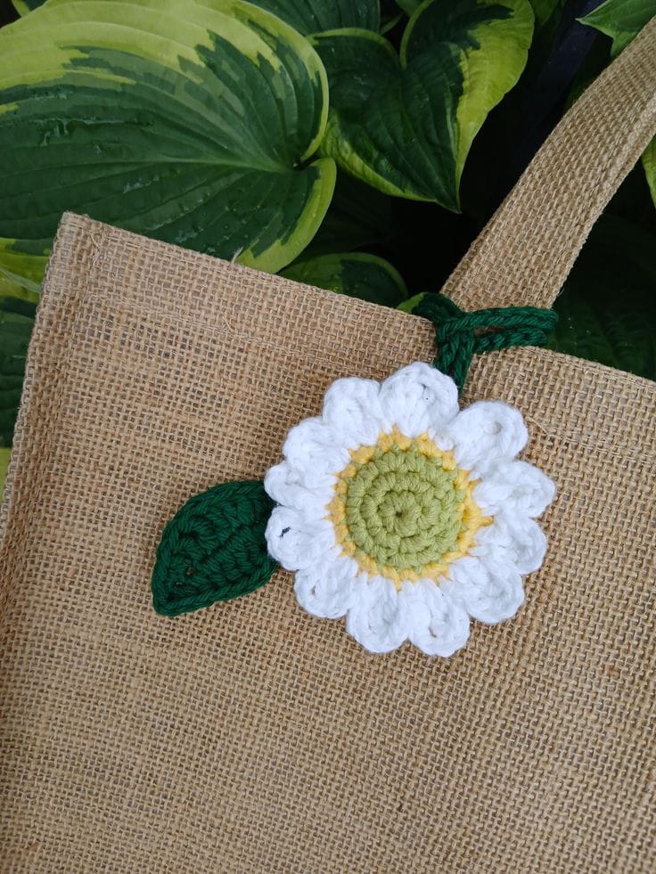 Handmade crochet sunflower bag charm with yellow petals and green leaves, hanging on a white tote with brown leather handle