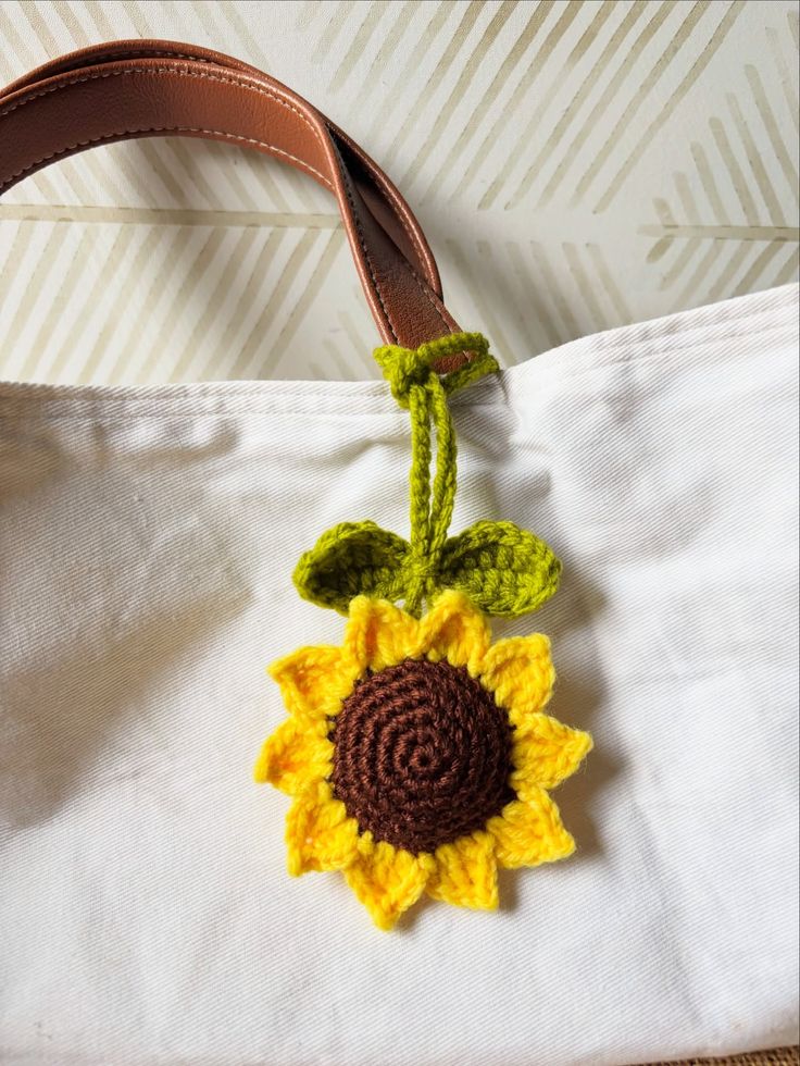 Handmade crochet sunflower bag charm with yellow petals and green leaves, hanging on a white tote with brown leather handle